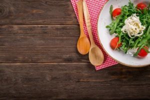 offset photo of salad on a placemat with wooden spoons on a rustic wooden table